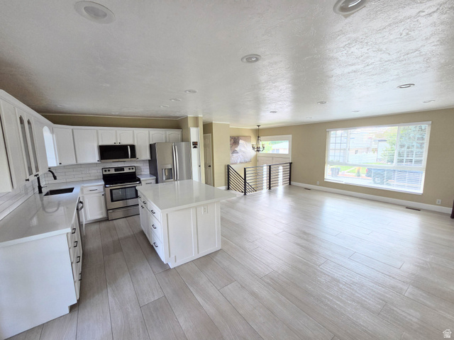 6123 Rodeo Lane Murray, UT 84121 - Photo 11 of 19 Open concept living space featuring a kitchen with white cabinetry and stainless steel appliances, a center island with a solid surface countertop, light wood-finish flooring, and recessed lighting