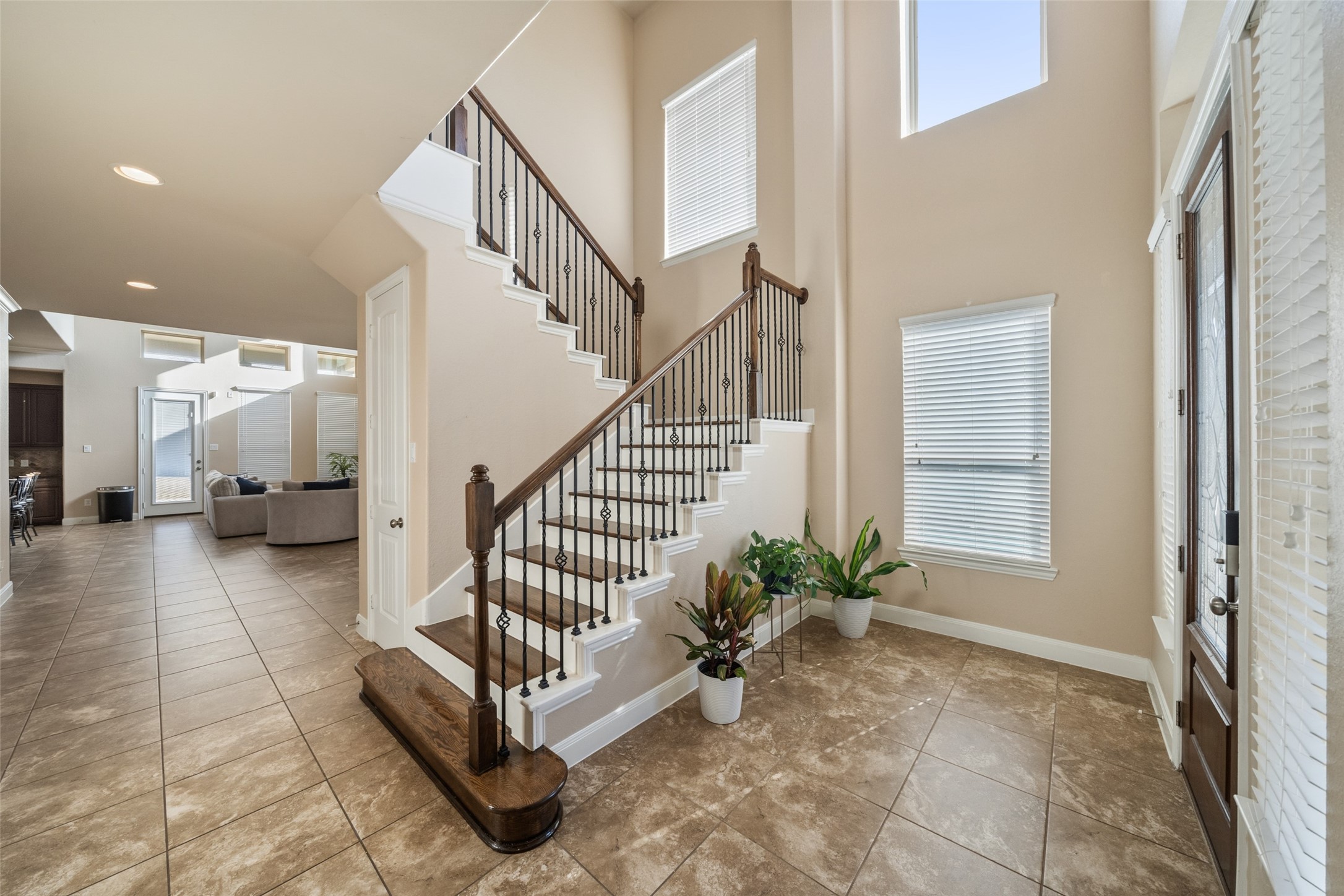 4747 Abercorn Street Rosharon, TX 77583 - Photo 4 of 46 This photo showcases a bright, spacious entryway with a stylish staircase featuring dark wood accents and wrought iron railings. The area is enhanced by large windows that let in ample natural light, and there's a view into an open-concept living space with tiled flooring and neutral-toned walls.