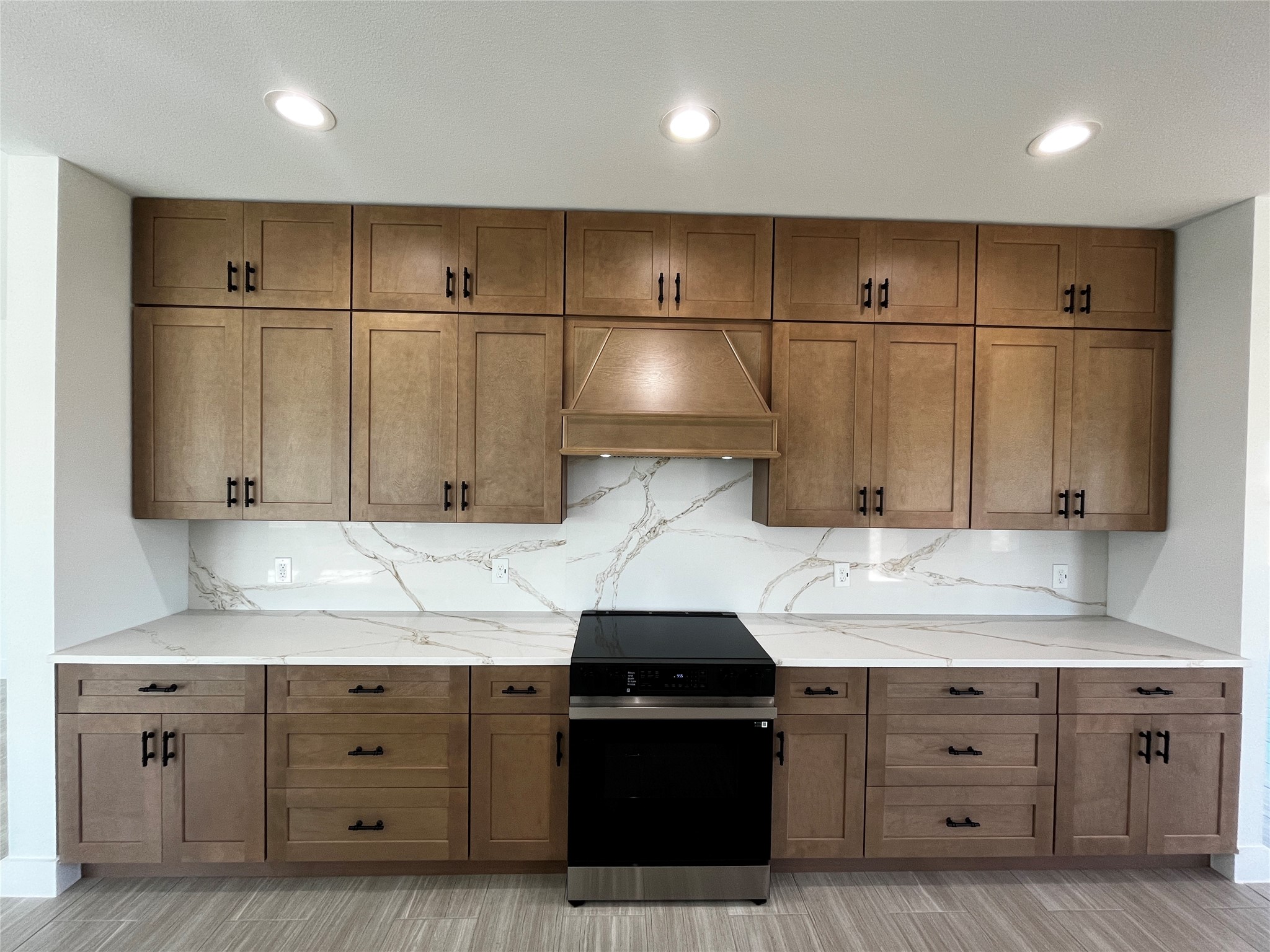 471 Buffalo Trail Angleton, TX 77515 - Photo 12 of 35 This kitchen features modern wooden cabinets with black handles, a sleek black stove, and elegant quartz countertops and backsplash. Recessed lighting enhances the clean, contemporary design.