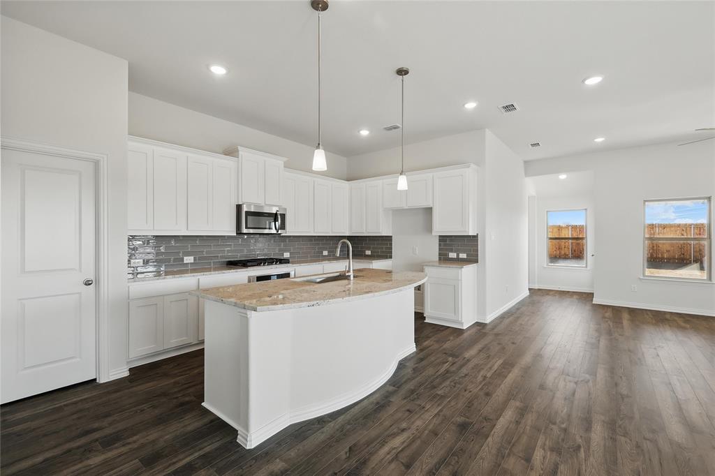 2529 Rivers W Road Anna, TX 75409 - Photo 3 of 22 Kitchen featuring a center island with sink, white cabinetry, light stone counters, stainless steel microwave, and dark wood-type flooring