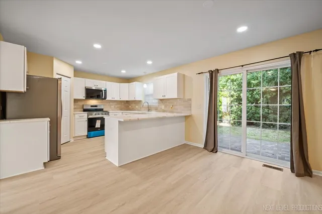 a kitchen with stainless steel appliances granite countertop a stove a sink a refrigerator white cabinets and wooden floor