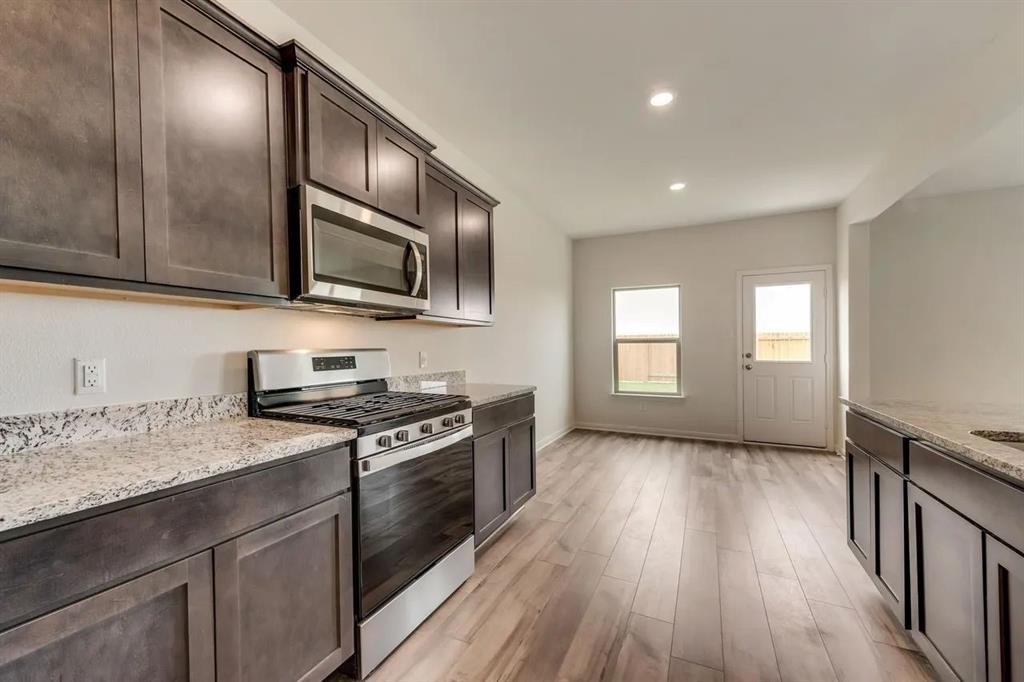 912 Mallorie Lane Ferris, TX 75125 - Photo 11 of 24 Kitchen with stainless steel appliances, dark brown cabinetry, light stone countertops, light wood-style flooring, and recessed lighting