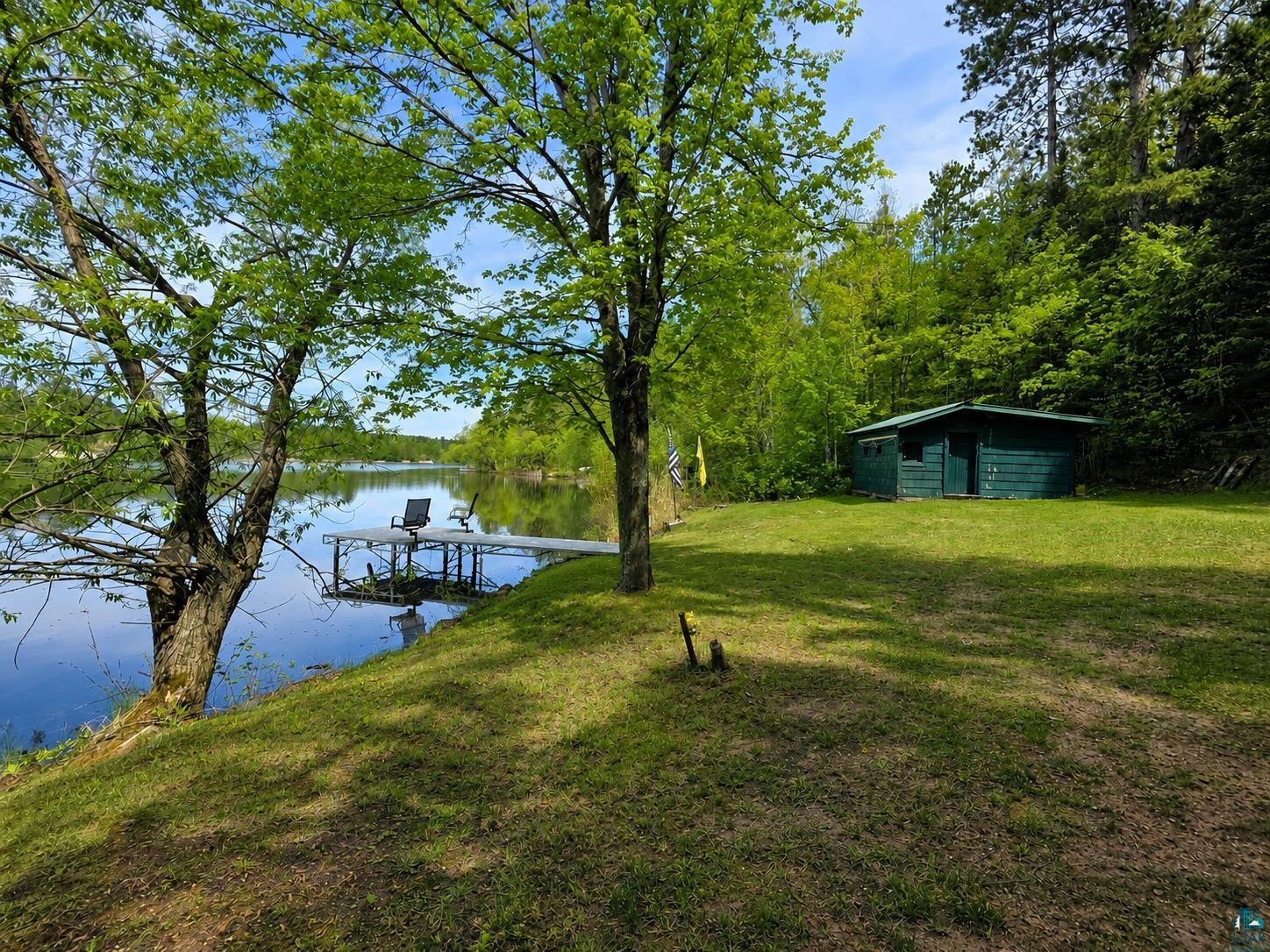 3975 Long Lake Shores Road Eveleth, MN 55734 - Photo 3 of 84 Waterfront property featuring a private dock, lush green lawn, mature trees, and a freestanding shed