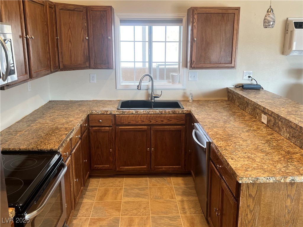 520 Burt Street Pahrump, NV 89060 - Photo 61 of 99 Kitchen featuring a peninsula, appliances with stainless steel finishes, pendant lighting, dark countertops, and brown cabinetry
