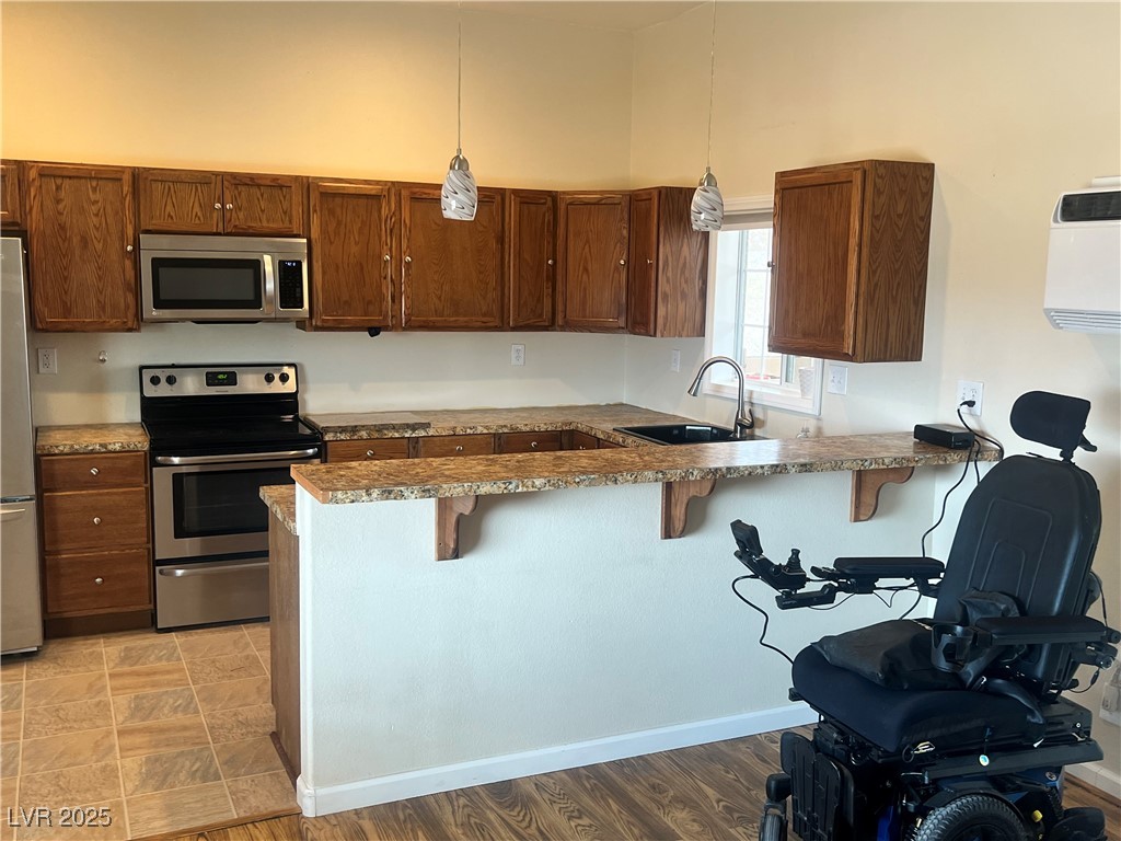 520 Burt Street Pahrump, NV 89060 - Photo 69 of 99 Kitchen featuring a kitchen bar, appliances with stainless steel finishes, hanging light fixtures, a peninsula, and brown cabinetry