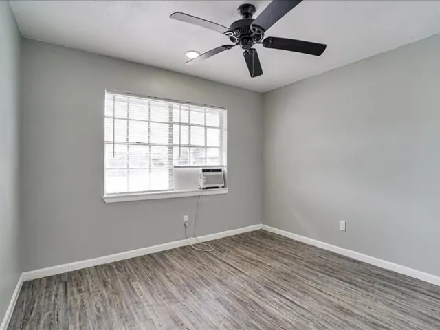 an empty room with wooden floor fan and windows