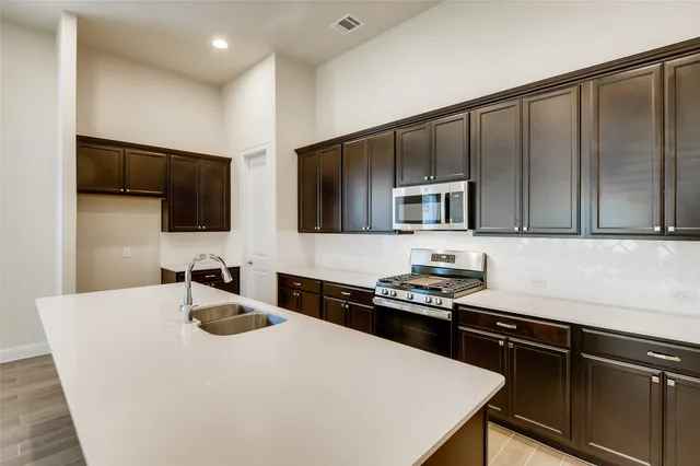 a kitchen with stainless steel appliances a sink dishwasher stove refrigerator and microwave with wooden floor
