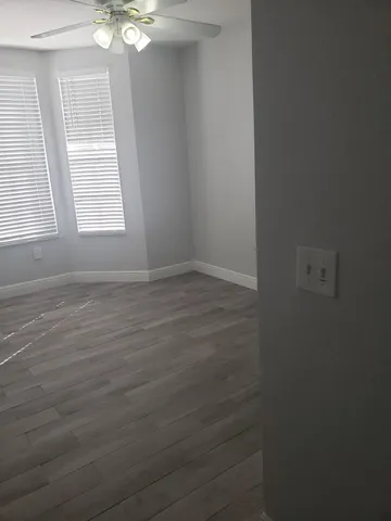an empty room with wooden floor fan and windows