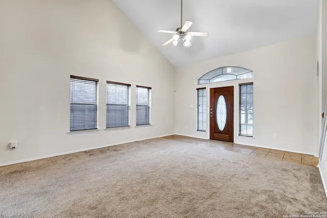 an empty room with chandelier fan and windows