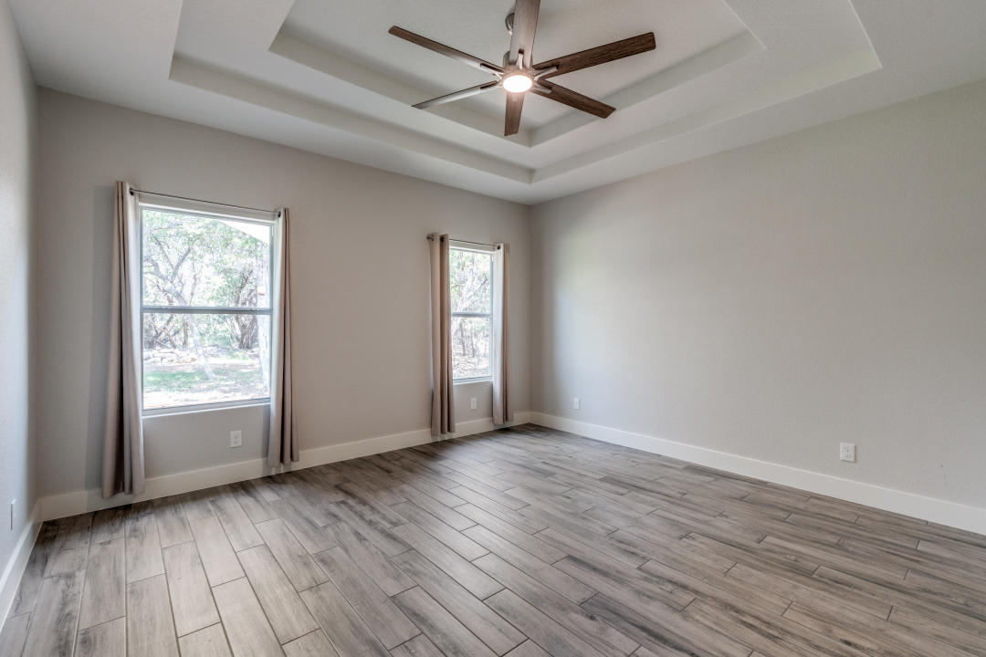 1848 Tanglewood Trail Spring Branch, TX 78070 - Photo 10 of 12 A spacious bedroom features tray ceilings, ample natural light, and stylish wood-look flooring.