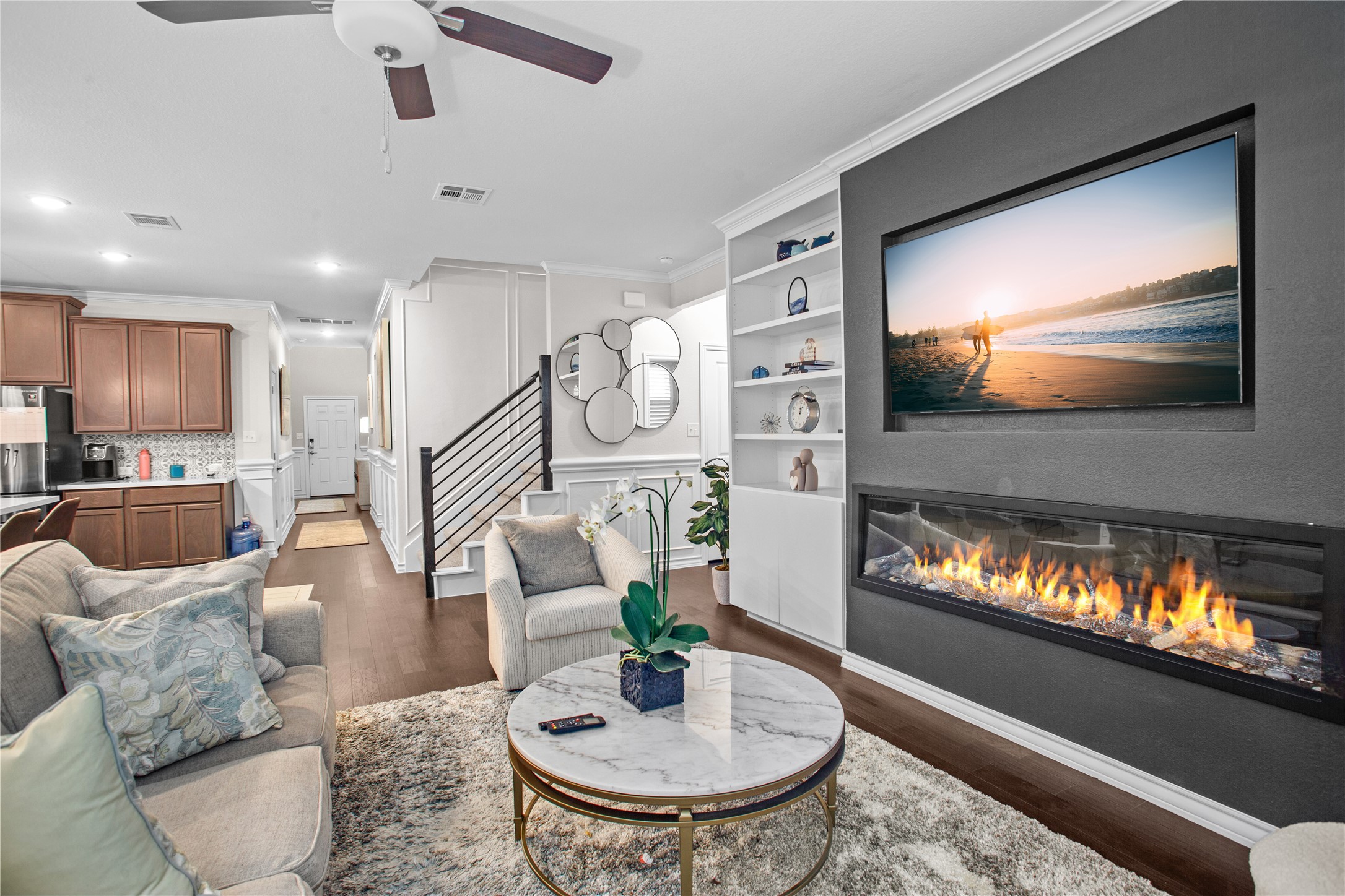 109 Adeline Road Hutto, TX 78634 - Photo 11 of 40 Living room featuring built in features, crown molding, dark wood-style flooring, ceiling fan, and a glass covered fireplace