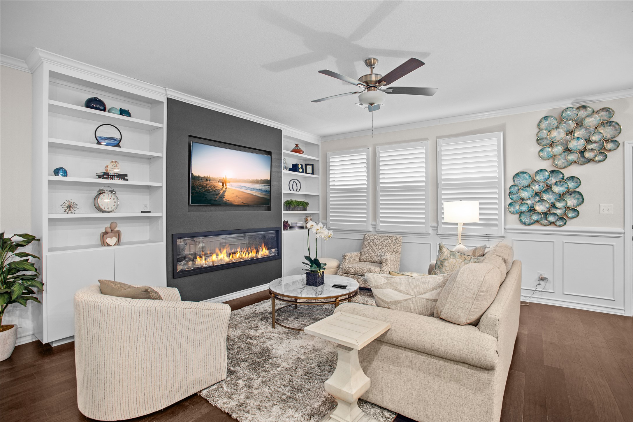 109 Adeline Road Hutto, TX 78634 - Photo 8 of 40 Living area featuring ornamental molding, dark wood finished floors, built in features, a glass covered fireplace, and a ceiling fan