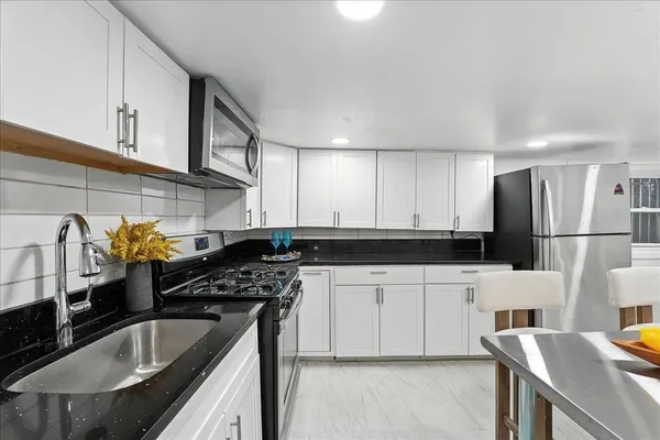 a kitchen with stainless steel appliances granite countertop a refrigerator a stove a dining table and chairs