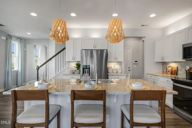 a kitchen with stainless steel appliances kitchen island granite countertop a dining table chairs and a refrigerator