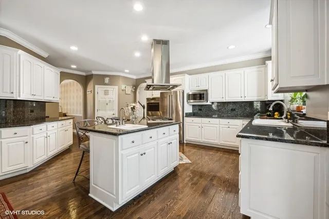 a kitchen with stainless steel appliances granite countertop a refrigerator a stove a sink dishwasher and white cabinets with wooden floor