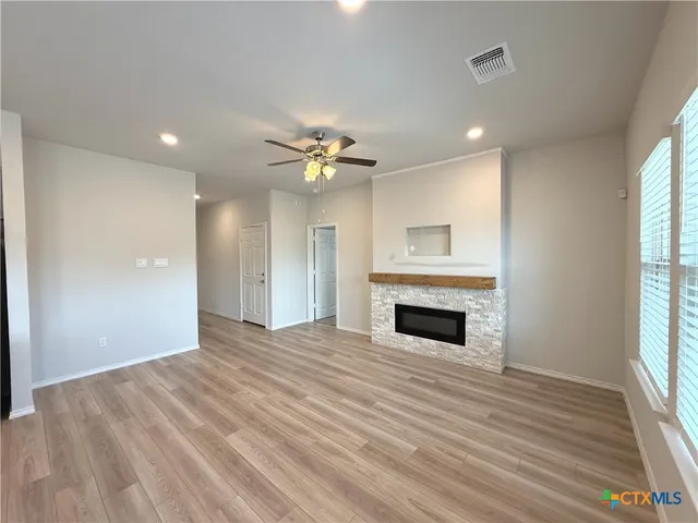 a view of an empty room with wooden floor fireplace and windows
