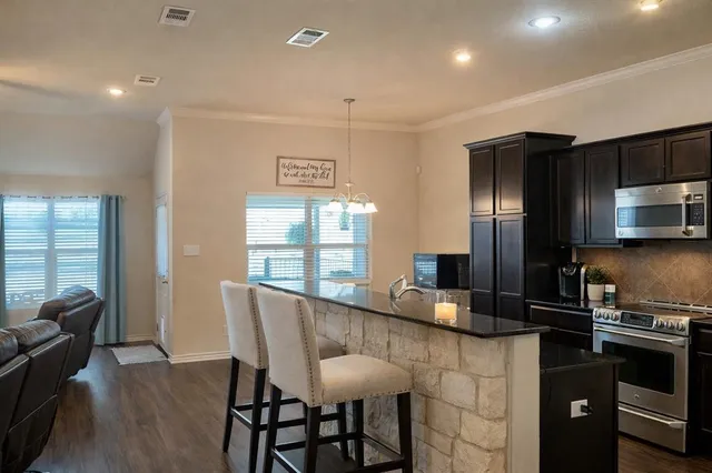 a kitchen with stainless steel appliances granite countertop a stove a refrigerator a sink a dining table and chairs