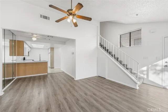 a view of an empty room with wooden floor and a kitchen view