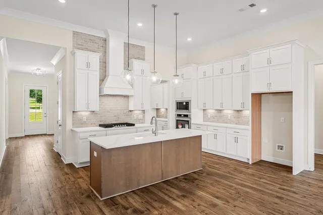 a large kitchen with stainless steel appliances kitchen island granite countertop a stove a refrigerator a sink and white cabinets with wooden floor