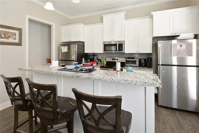 a kitchen with stainless steel appliances granite countertop a dining table chairs refrigerator and sink
