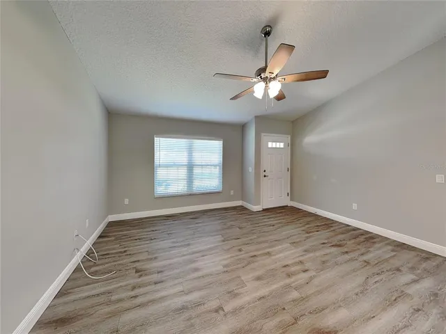 an empty room with wooden floor ceiling fan and window