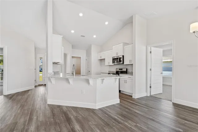 a large white kitchen with kitchen island a sink a stove a refrigerator and white cabinets with wooden floor