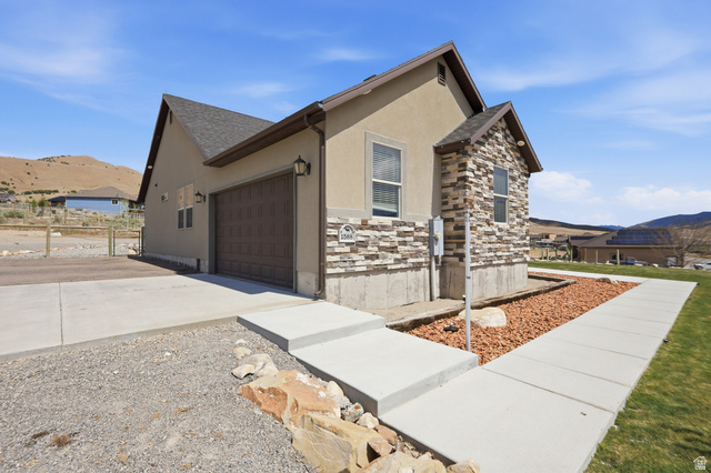 1588 West Rim Rock Drive Stockton, UT 84071 - Photo 53 of 61 Contemporary exterior featuring a textured stucco finish, stone veneer accents, an attached garage with a panel door, a concrete driveway, and a concrete pathway leading to the entrance