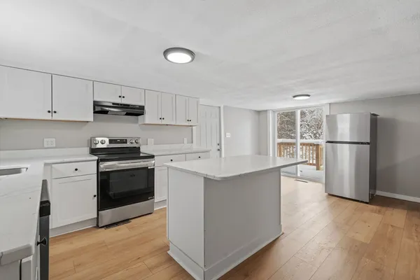 a kitchen with stainless steel appliances granite countertop a refrigerator a stove a sink and white cabinets with wooden floor