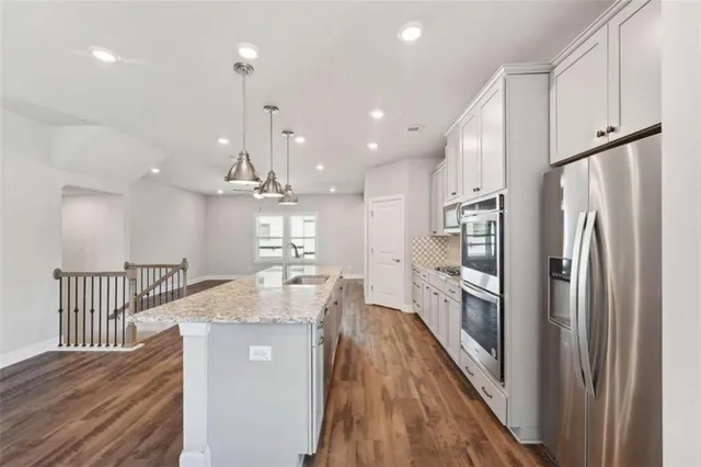 a kitchen with stainless steel appliances granite countertop a refrigerator a sink dishwasher a stove and white cabinets with wooden floor