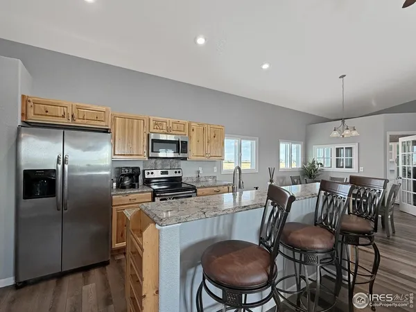 a kitchen with stainless steel appliances granite countertop a refrigerator a stove a sink a dining table and chairs with wooden floor