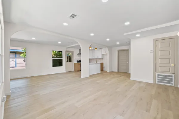 an empty room with wooden floor kitchen and windows