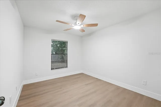 an empty room with wooden floor ceiling fan and windows