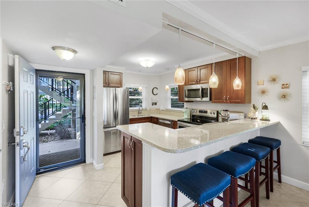 201 Quail Forest Boulevard, Unit 101 Naples, FL 34105 - Photo 14 of 32 a kitchen with stainless steel appliances a table chairs refrigerator and microwave