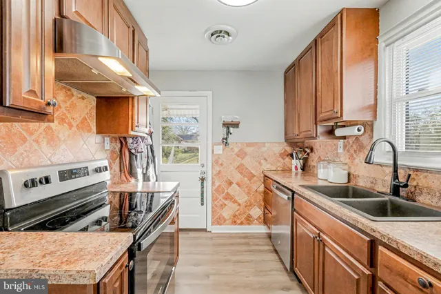 a kitchen with stainless steel appliances granite countertop a refrigerator a stove and a sink with wooden floor