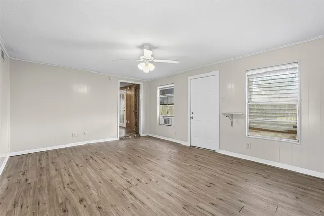 an empty room with wooden floor chandelier fan and windows
