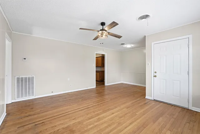 a view of an empty room with wooden floor and a ceiling fan