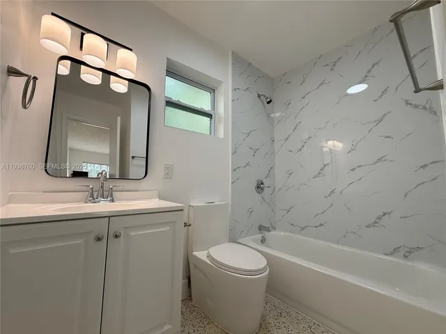 a bathroom with a toilet a sink a mirror a bathtub and vanity