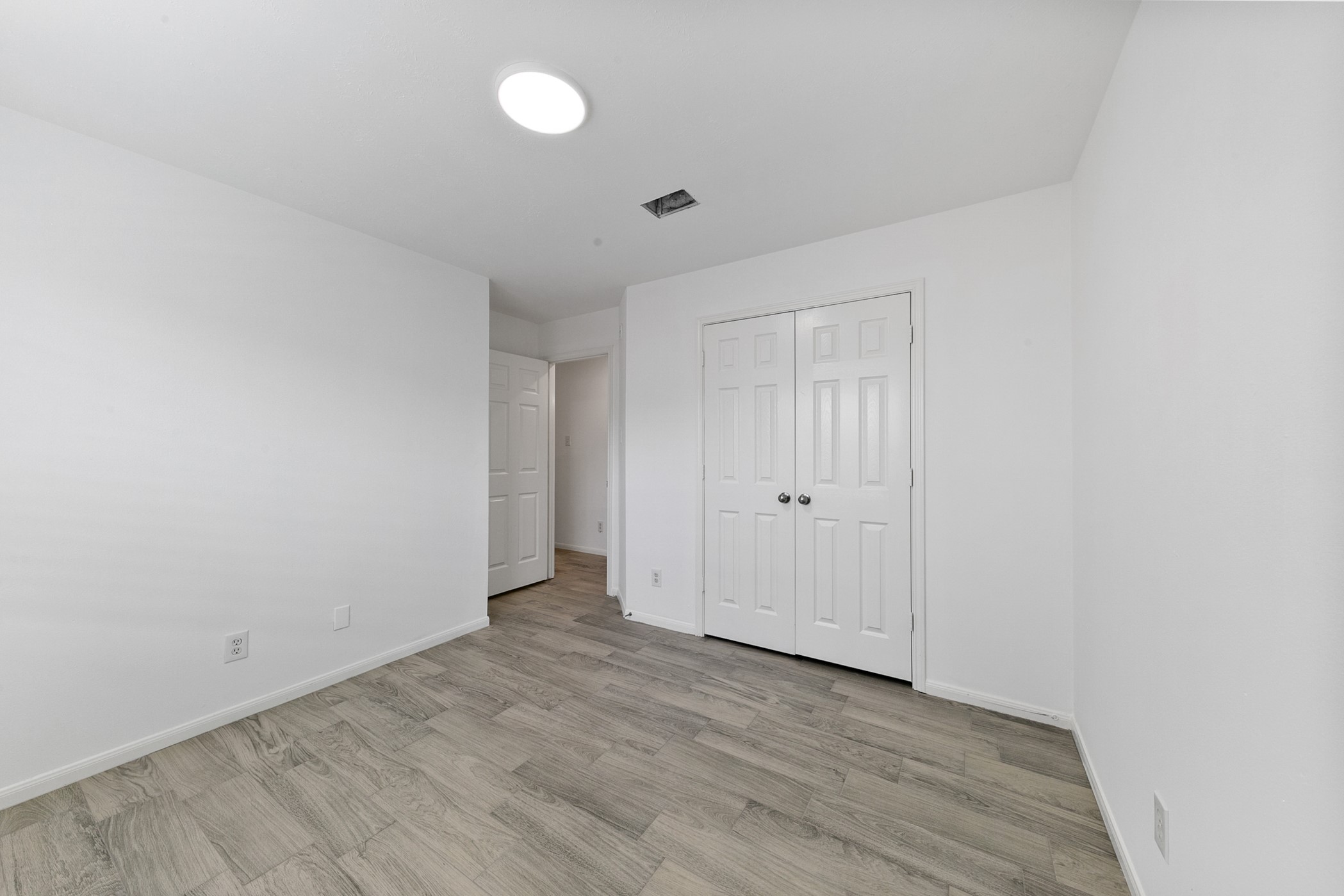 12014 Raven View Drive Houston, TX 77067 - Photo 9 of 29 This photo shows a bright, unfurnished room with light wood flooring and white walls. It features a double-door closet and a ceiling light, ideal for a bedroom or office space.