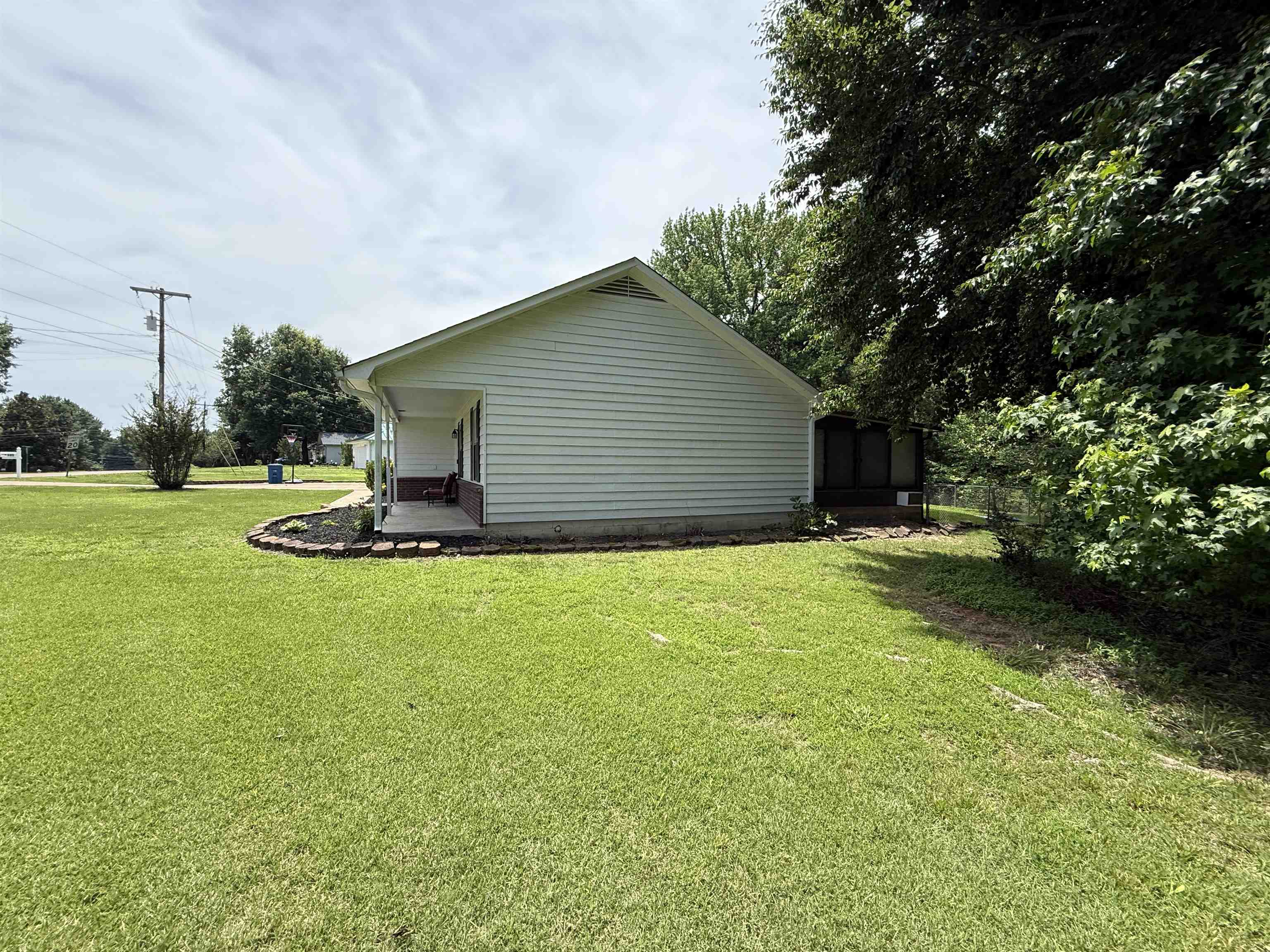 185 Mignon Road Atoka, TN 38004 - Photo 9 of 34 White vinyl siding exterior with a covered front porch featuring stone-look flooring, a curved landscape bed, and mature perimeter trees