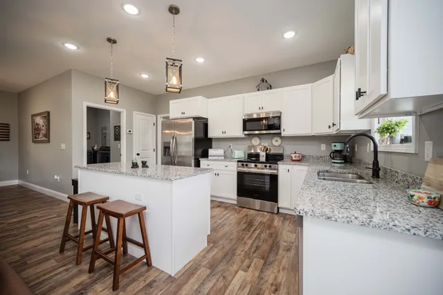 a kitchen with stainless steel appliances granite countertop a refrigerator oven a sink a stove a dining table and chairs with wooden floor