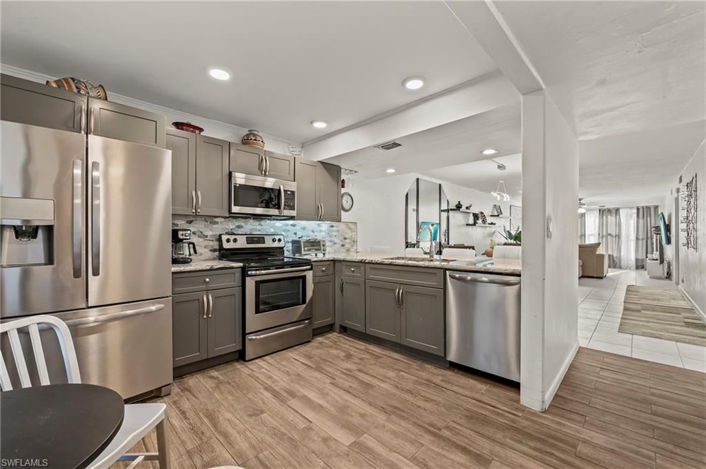 Kitchen with gray cabinets, backsplash, a sink, stainless steel appliances, and light wood-style floors