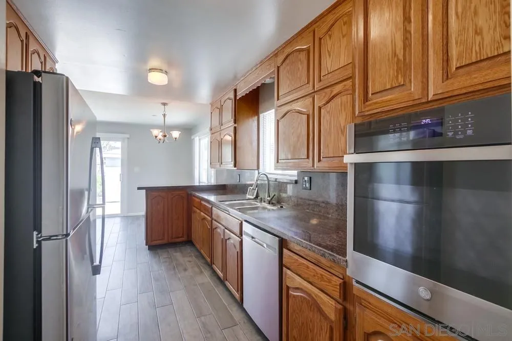 a kitchen with stainless steel appliances granite countertop a refrigerator a sink dishwasher and wooden cabinets with wooden floor