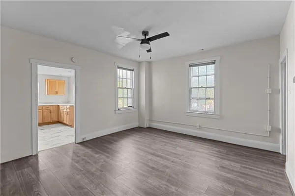 an empty room with wooden floor ceiling fan and windows