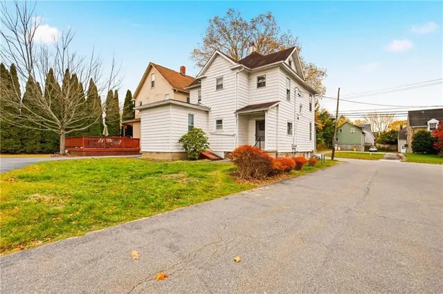 a view of a white house with a small yard and large trees