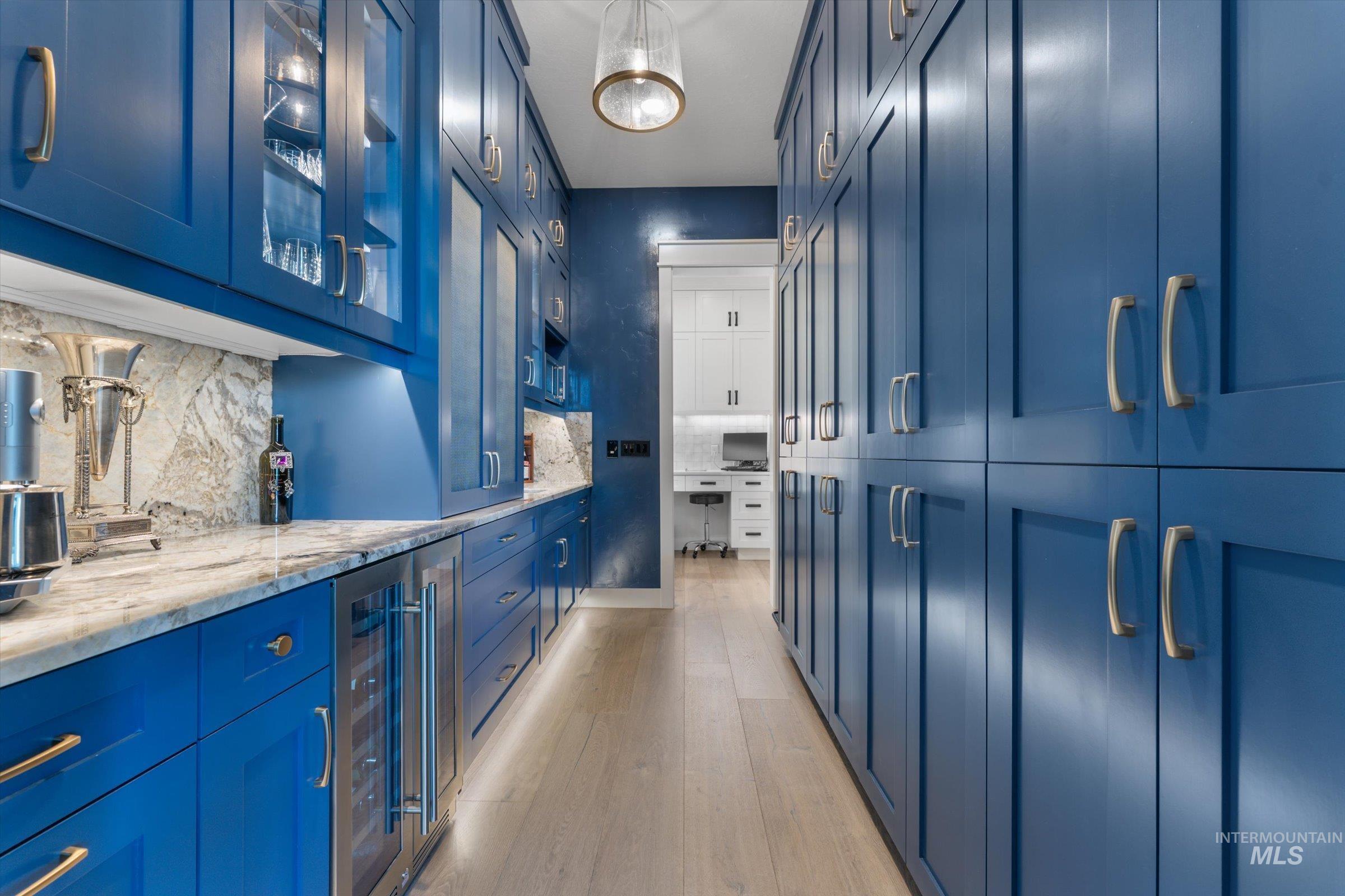 6585 South Pemberley Way Meridian, ID 83642 - Photo 20 of 43 Galley-style pantry featuring extensive custom blue cabinetry, wood-finish flooring, stone countertops with matching backsplash, built-in wine cooler, and integrated under-cabinet lighting