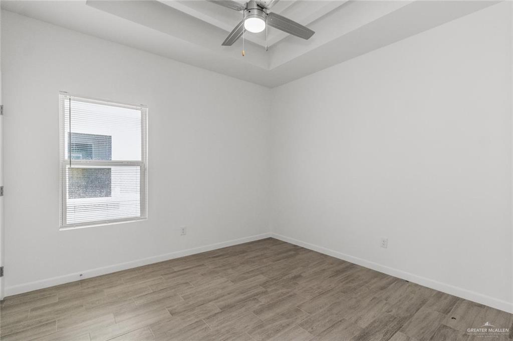 304 West Campeche Avenue, Unit 3 Alton, TX 78573 - Photo 2 of 10 Unfurnished room featuring light wood-style floors, baseboards, ceiling fan, and a tray ceiling