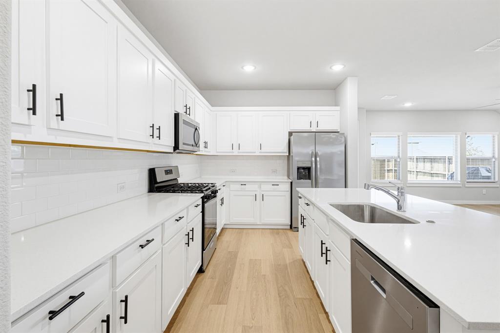 Modern kitchen featuring white shaker cabinetry, stainless steel appliances, light wood-finish flooring, white subway tile backsplash, and an island with an undermount sink