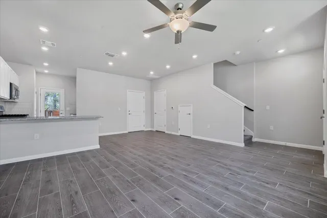 a view of an empty room with wooden floor and kitchen