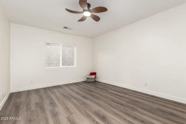an empty room with wooden floor fan and windows