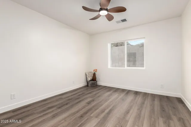 an empty room with wooden floor chandelier fan and windows
